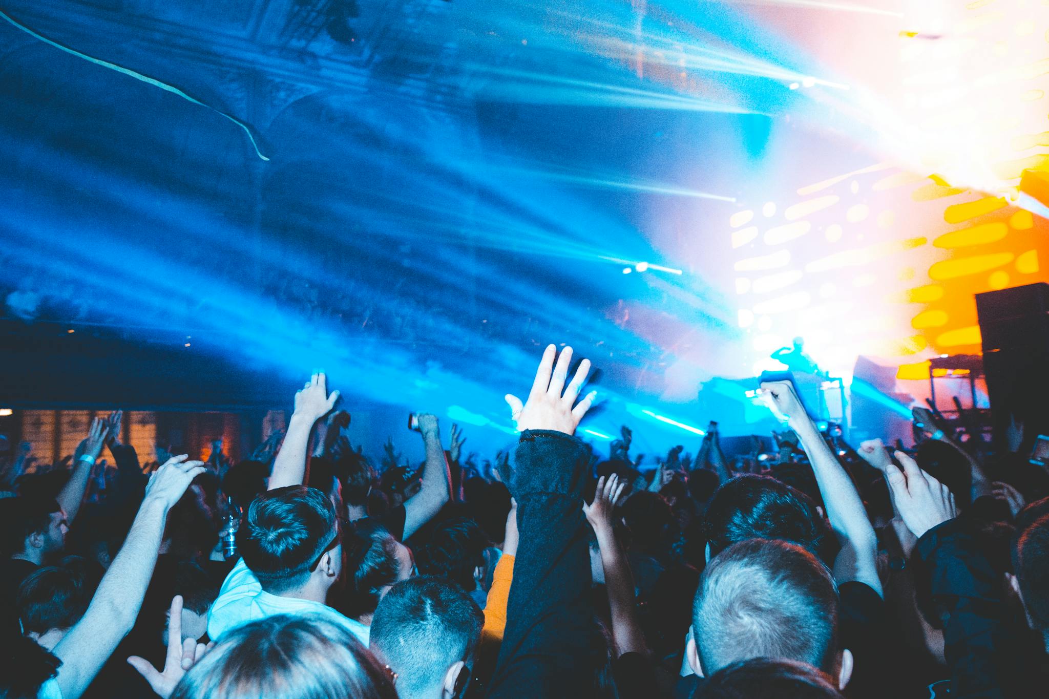 Excited nightclub crowd raising hands in vibrant lights, enjoying a live DJ set. Perfect for nightlife and music culture visuals.